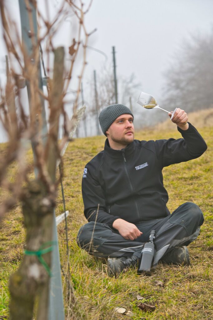 Johannes Stuttner sitzend im Weingarten mit dem Weinglas in der Hand.
